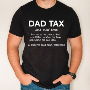 May include: Black t-shirt with white text that reads "DAD TAX /dad taks/ noun 1. Portion of an item a dad is entitled to when he buys something for his kids. 2. Ensures food isn't poisonous"