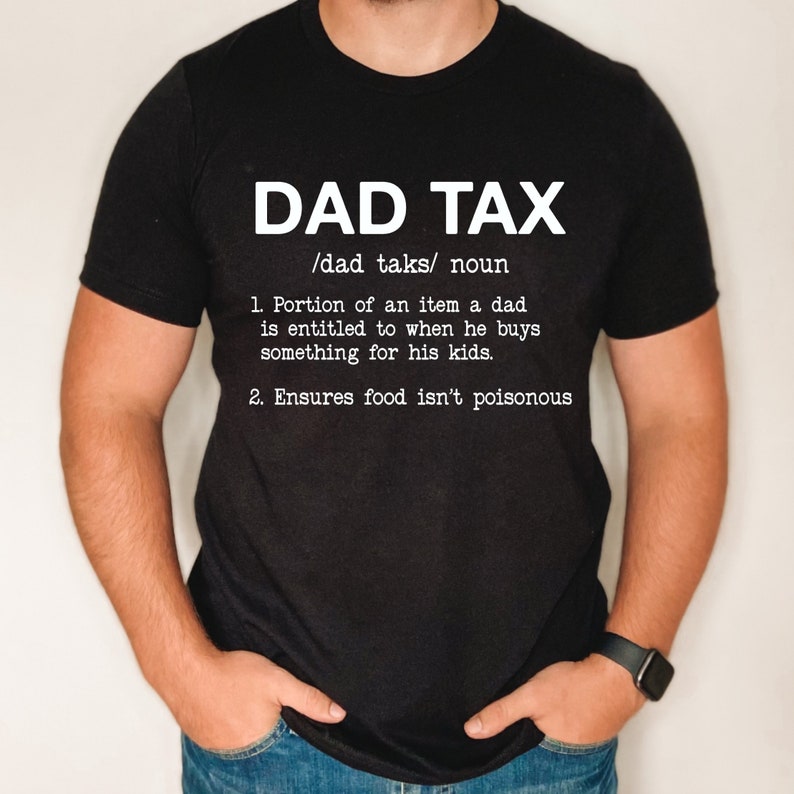 May include: Black t-shirt with white text that reads "DAD TAX /dad taks/ noun 1. Portion of an item a dad is entitled to when he buys something for his kids. 2. Ensures food isn't poisonous"