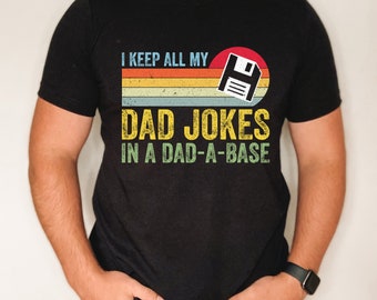 May include: Black t-shirt with a vintage-style graphic that says "I keep all my dad jokes in a dad-a-base" with a floppy disk icon.