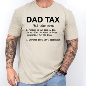 May include: A beige t-shirt with the text "DAD TAX /dad taks/ noun 1. Portion of an item a dad is entitled to when he buys something for his kids. 2. Ensures food isn't poisonous"