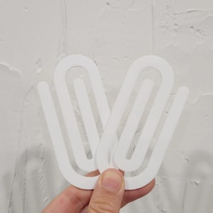 May include: Two white plastic curtain clips, designed to hold curtains in place. The clips are shaped like a large paperclip.