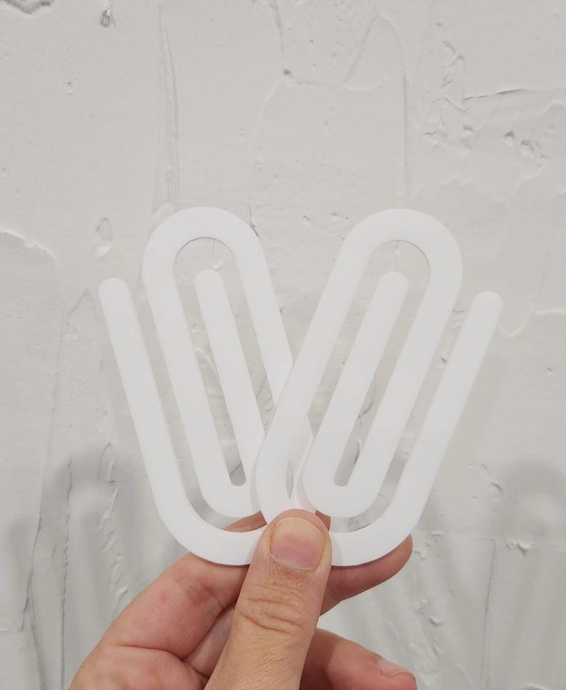May include: Two white plastic curtain clips, designed to hold curtains in place. The clips are shaped like a large paperclip.