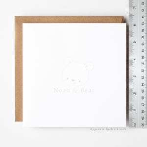 Puede incluir: Una tarjeta de felicitaci&oacute;n cuadrada de color blanco con un dibujo de l&iacute;neas gris claro de una cara de oso y el texto Noah & Bear. Un sobre marr&oacute;n se coloca detr&aacute;s de la tarjeta. Una regla met&aacute;lica muestra que la tarjeta mide unos 15 cm por 15 cm.