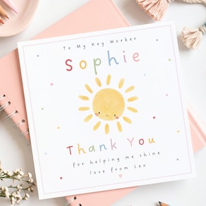 May include: A square greeting card featuring a watercolour yellow sun with a smiling face in the centre. The text reads To My Key Worker Sophie, Thank You for helping me shine, love from Leo. The design includes small colourful stars on a white background.