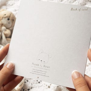 Puede incluir: Una tarjeta cuadrada blanca con el texto Back of card en la esquina superior derecha. El centro muestra un dibujo lineal de una cara de oso sobre el texto Noah & Bear, for life's sweetest chapters, direcciones web y un peque&ntilde;o coraz&oacute;n.
