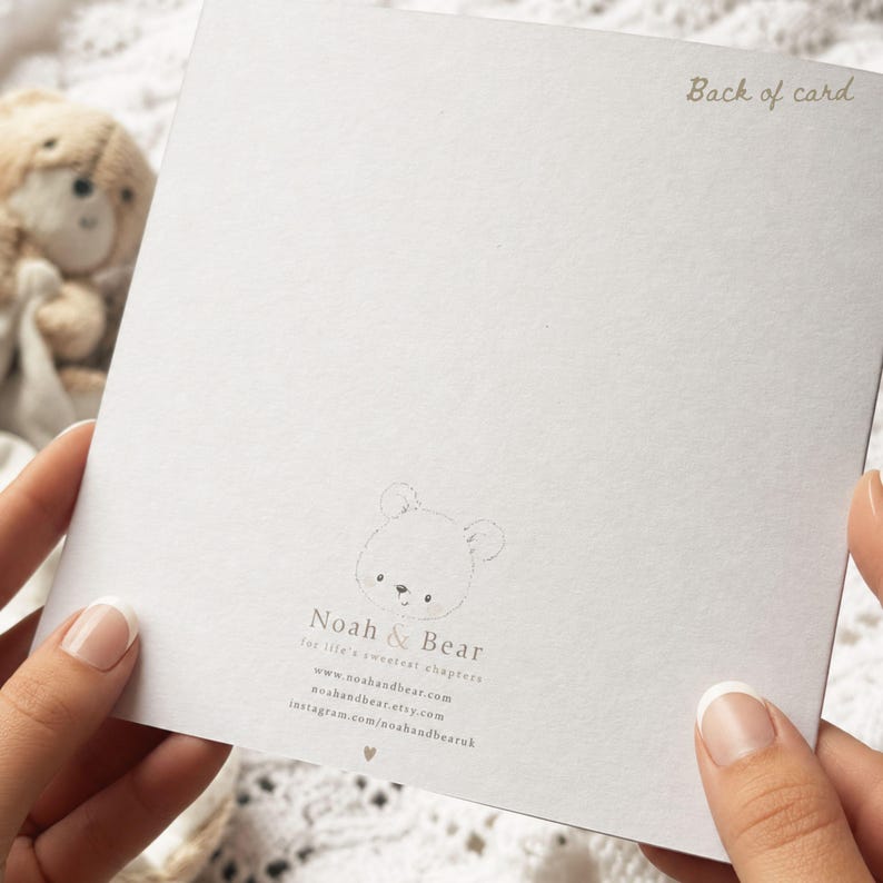 Puede incluir: Una tarjeta cuadrada blanca con el texto Back of card en la esquina superior derecha. El centro muestra un dibujo lineal de una cara de oso sobre el texto Noah & Bear, for life's sweetest chapters, direcciones web y un peque&ntilde;o coraz&oacute;n.