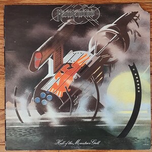 May include: A vintage vinyl record album cover featuring a futuristic, mechanical design in shades of gray, orange, and blue. The album is titled "Hall of the Mountain Grill" by the band "Hawkwind".
