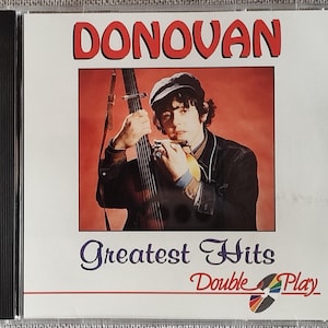 May include: CD case featuring Donovan's "Greatest Hits" album. The cover art shows Donovan holding a musical instrument, with the title in red letters at the top. The words "Greatest Hits" and "Double Play" are also visible.