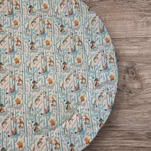 May include: A round, blue and white fabric play mat with a repeating pattern of rabbits and trees. The mat is perfect for babies and toddlers to play on.