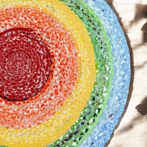 May include: A colourful round rug made from woven fabric scraps. The rug has a concentric circle design with shades of red, orange, yellow, green, and blue.