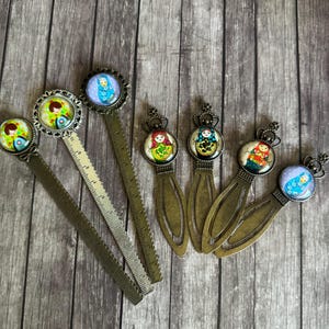 Puede incluir: Conjunto de siete marcapáginas de metal con diferentes diseños que representan muñecas rusas. Los marcapáginas son en tonos dorados, azules, verdes, rojos y amarillos. Algunos marcapáginas tienen una regla en el lateral.