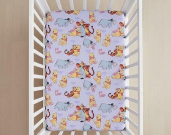 May include: A fitted cot sheet with a repeating pattern of Winnie the Pooh, Tigger, Eeyore, and Piglet on a lavender background. The sheet is inside a white cot.
