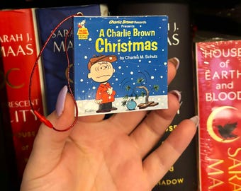 May include: A blue and white book with a picture of Charlie Brown on the cover. The book is titled "A Charlie Brown Christmas" and is a read-along record book. The book is being held in a hand.