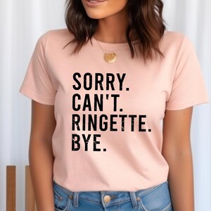 May include: A pink t-shirt with the text "SORRY. CAN'T. RINGETTE. BYE." printed in black.