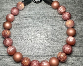 May include: A rose gold beaded necklace with a black metal clasp. The beads are round and have a shimmery finish.