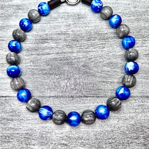 May include: A blue and gray beaded necklace with a silver metal clasp. The beads are round and have a marbled pattern.