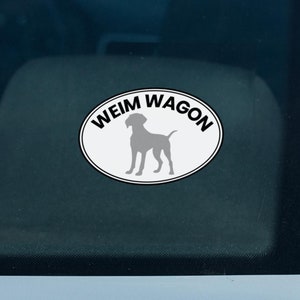 Puede incluir: Una pegatina ovalada blanca con texto negro que dice "Weim Wagon" y una silueta gris de un perro Weimaraner en su interior.