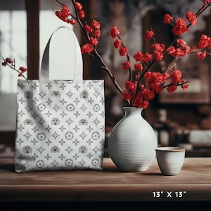 Puede incluir: Una bolsa de tela blanca con un patrón gris y blanco de perros pequeños y flores. La bolsa mide 13 pulgadas por 13 pulgadas.