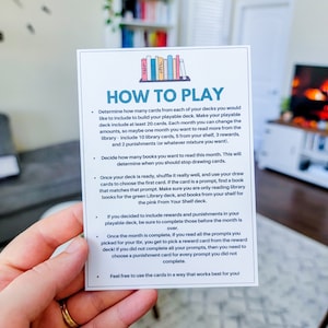 May include: A white card with blue and green text and illustrations of books. The card has instructions on how to play a reading game. The text on the card reads "How to Play".