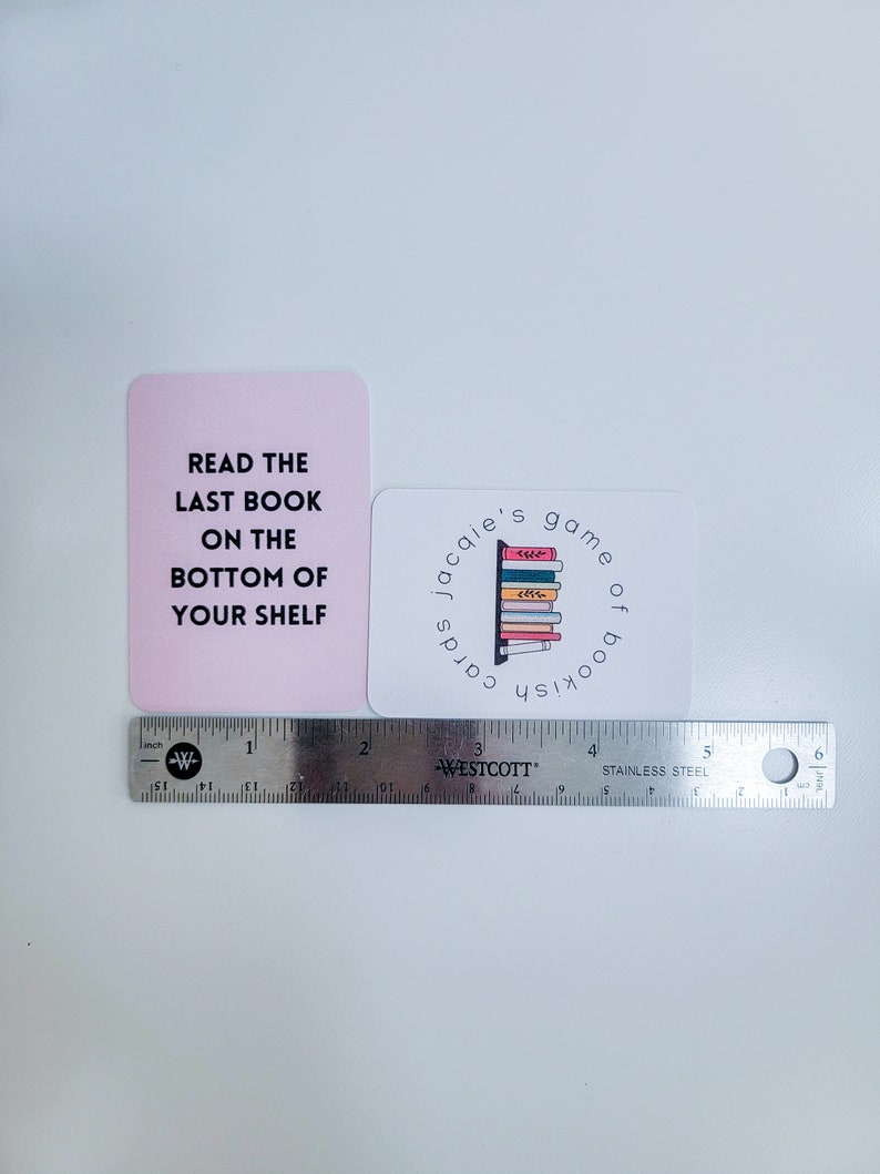 May include: Two pink and white cards with text that reads "Read the last book on the bottom of your shelf" and "Jacquie's game of bookish cards". The second card has a graphic of a bookshelf with colourful books.