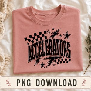 Puede incluir: Una camiseta de color rosa polvoriento con un estampado gráfico negro que muestra la palabra ACCELERATORS en una fuente arqueada y negrita. El diseño incluye patrones de cuadros en blanco y negro, rayos y estrellas alrededor del texto.