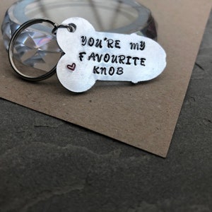 May include: Silver keychain shaped like a knob with the text "You're my favourite knob" and a small red heart.