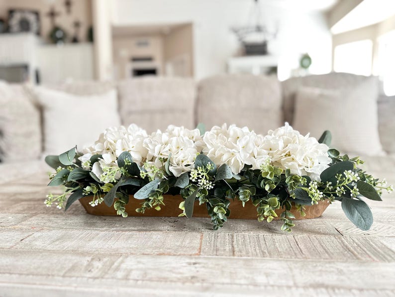 May include: A wooden trough centerpiece filled with white hydrangeas and green eucalyptus leaves.