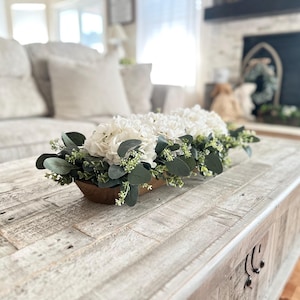May include: A white wooden coffee table with a white and green floral arrangement in a wooden trough.