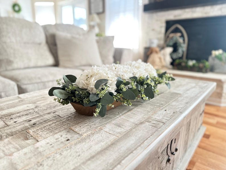 May include: A white wooden coffee table with a white and green floral arrangement in a wooden trough.