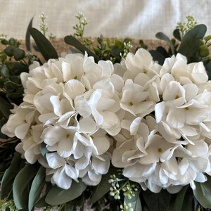 May include: A white hydrangea floral garland with green eucalyptus leaves. The garland is perfect for adding a touch of greenery and elegance to any space.