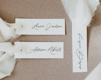 May include: Three white rectangular place cards with black calligraphy. The cards read "Laura Jackson", "Allison Roberts", and "Evelyn Bryant".
