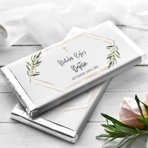 May include: Two chocolate bars wrapped in silver foil, with white paper labels. The labels feature a gold geometric frame, a cross, olive branch illustrations, and the text "Nicholas Kyle's Baptism, September 24th, 2022."
