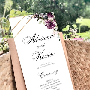 May include: Wedding ceremony program with a floral design featuring purple and white flowers. The program lists the order of events for the ceremony, including the prelude, seating of the families, bridal processional, and recessional.