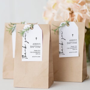 May include: Kraft paper gift bags with white tags. The tags read "Thank you" and "ADRIAN'S BAPTISM" with a cross symbol and the date August 19, 2025. Each tag is adorned with a sprig of greenery.