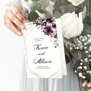 May include: Wedding invitation featuring a gold geometric frame and watercolour floral design in shades of purple and green. The text reads "Welcome to the Wedding of Kevin and Allison, September 25, 2021, San Francisco, California."