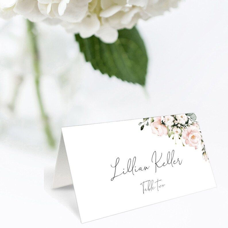 Puede incluir: Tarjeta de lugar blanca con un dise&ntilde;o floral en tonos rosa y verde. El texto "Lillian Keller" y "Mesa Dos" est&aacute; impreso en negro.