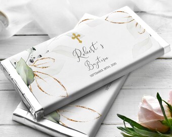 May include: Two silver foil-wrapped chocolate bars with a white background featuring a gold cross, green and white leaves, and gold glitter. The text on the bar reads "Robert's Baptism September 28th, 2020".