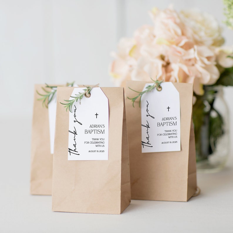 May include: Kraft paper gift bags with white tags. The tags read "Thank you" and "ADRIAN'S BAPTISM" with a cross symbol and the date August 19, 2025. Each tag is adorned with a sprig of greenery.