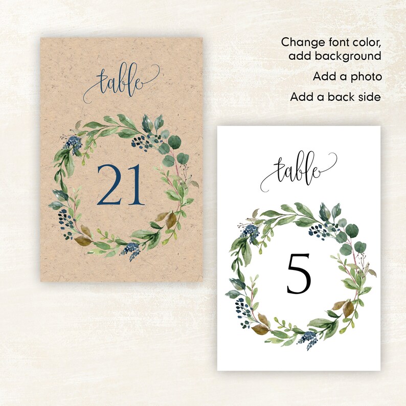 May include: Two table number cards with a watercolor wreath design. The first card has a brown background and the number 21. The second card has a white background and the number 5. Both cards have the text "table" in cursive.