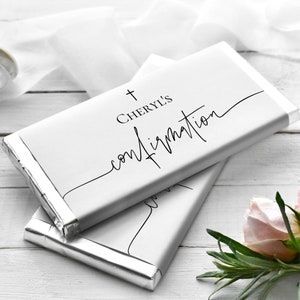 May include: Two silver foil-wrapped chocolate bars with a white label. The label has a cross and the text "CHERYL'S Confirmation" in black cursive.
