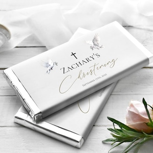 Puede incluir: Envoltorio de chocolate blanco con una cruz dorada, dos palomas blancas y el texto "Zachary's Christening September 17th, 2025".