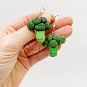 Może przedstawiać: Para zielonych kolczyków w kształcie brokuła z uśmiechniętą buźką. Kolczyki są wykonane z polimerowej gliny i mają srebrne haczyki.