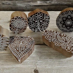 Puede incluir: Colección de sellos de bloques de madera con intrincados diseños blancos. Los sellos presentan patrones florales, de hojas, de corazón y mandala. Los bloques son de varias formas y tamaños, perfectos para manualidades y añadir elementos decorativos.