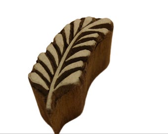 May include: A wooden block printing stamp with a carved design of a single leaf. The stamp is brown and the leaf design is white.