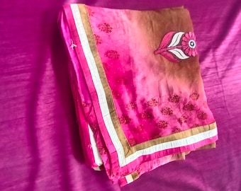 Könnte beinhalten: Ein gefaltetes Textil mit einem Farbverlauf von tiefem Magenta zu einem gedämpften Braun. Der Rand ist mit weißen und goldfarbenen Streifen akzentuiert. Ein gesticktes blattförmiges Motiv in Pink, Weiß und Schwarz ist auf der Oberfläche zu sehen.