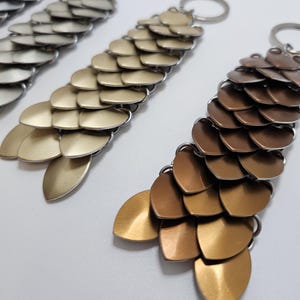 May include: Three metal keychains with a dragon scale design. The keychains are gold, silver, and bronze.