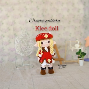 May include: A handmade crochet doll, featuring a red hat and dress with white and brown accents. The doll has blonde yarn hair and is labeled "Klee doll" and "Crochet pattern". The doll is standing in front of a floral background.