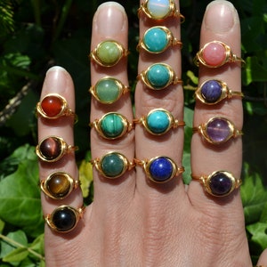 Peut inclure: Une main portant 14 bagues en or avec des pierres précieuses de différentes couleurs. Les bagues sont faites de fil enroulé autour des pierres.