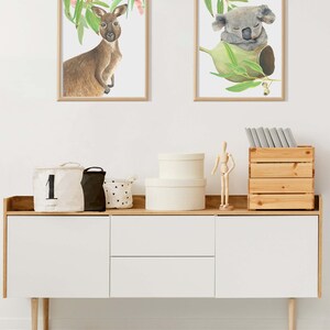 May include: Two framed watercolor prints of Australian animals: a kangaroo and a koala. The kangaroo is brown and the koala is gray. The prints are displayed above a white cabinet with wooden accents, and a striped rug.