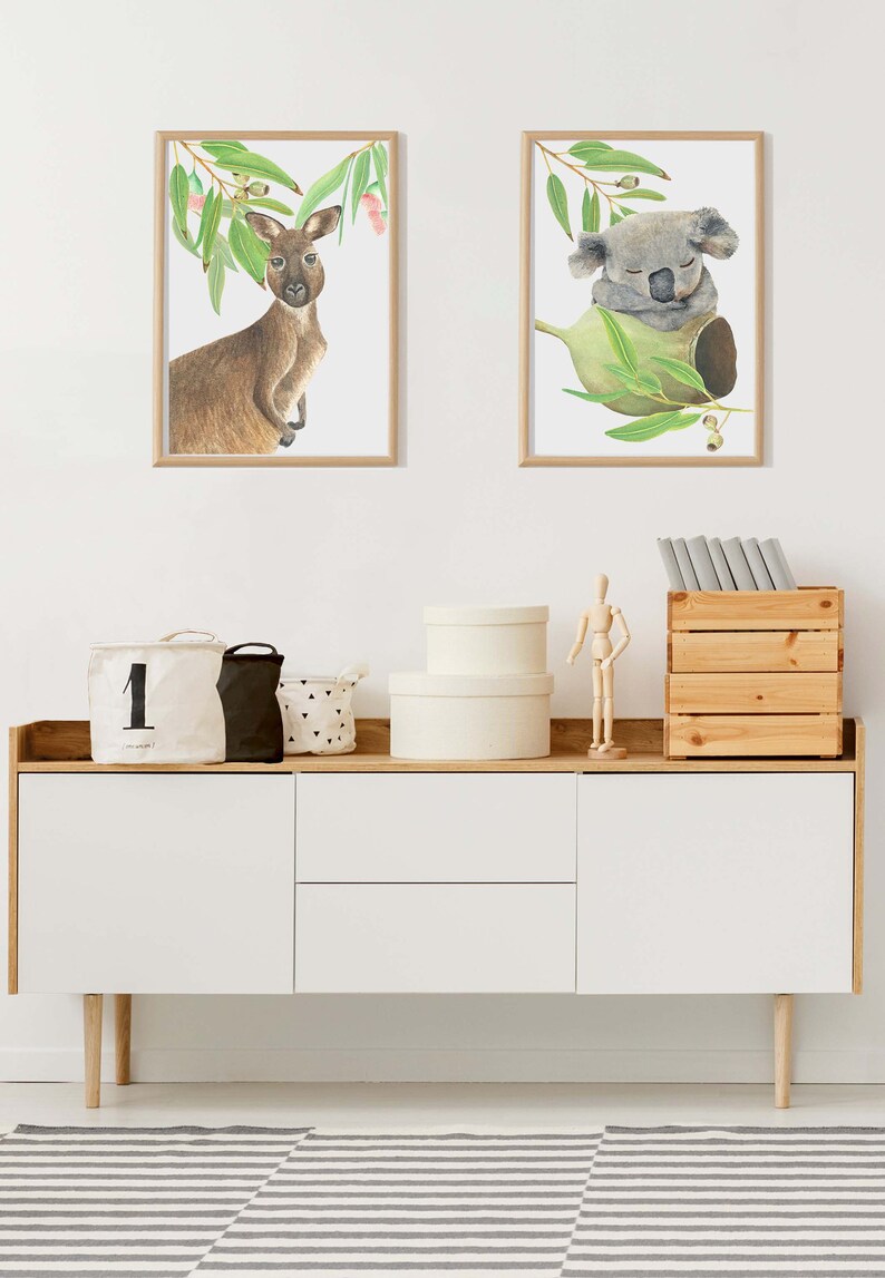 May include: Two framed watercolor prints of Australian animals: a kangaroo and a koala. The kangaroo is brown and the koala is gray. The prints are displayed above a white cabinet with wooden accents, and a striped rug.